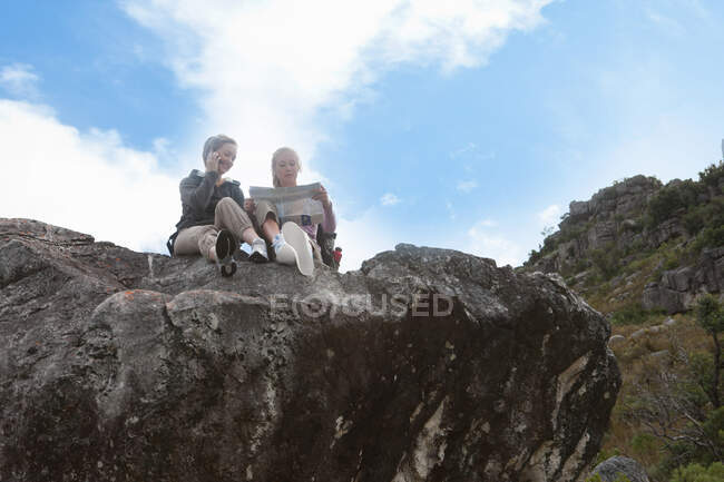 Duas garotas caminhantes lendo mapa no topo da formação rochosa — Fotografia de Stock