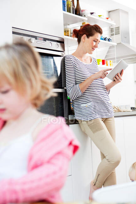 Mother using digital tablet, daughter in foreground — Stock Photo