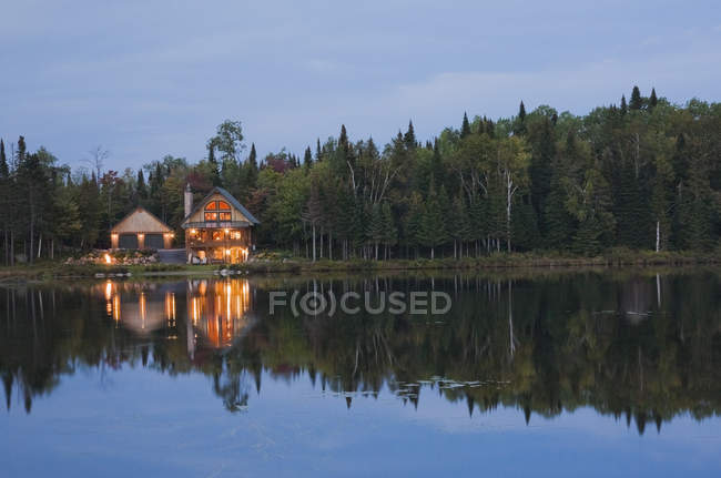 Illuminated garage and handcrafted spruce log home — Stock Photo