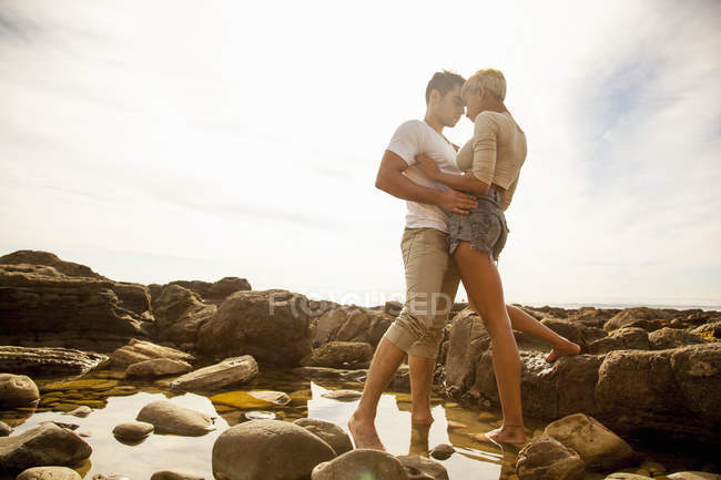 Молода пара стоїть разом, обличчям до обличчя, в кам'яному басейні на пляжі — стокове фото