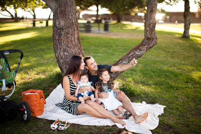 Familia con dos niños sentados en una manta de picnic - foto de stock
