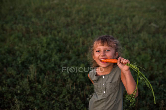 Портрет молодой девушки, поедающей свежесобранную морковку — стоковое фото