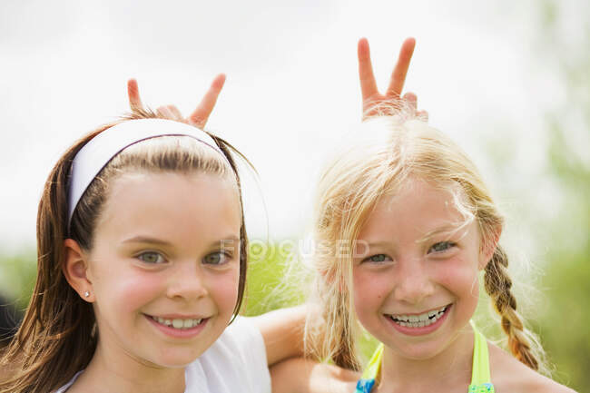 2 chicas jóvenes sonriendo dando orejas de conejo - foto de stock