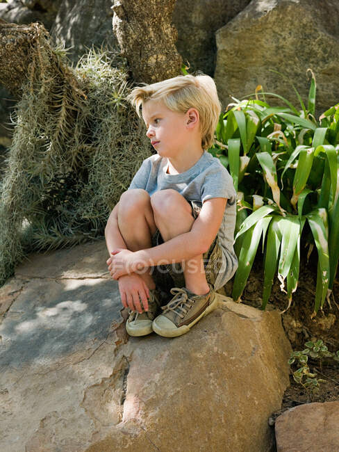Niño pensativo sentado en la roca - foto de stock