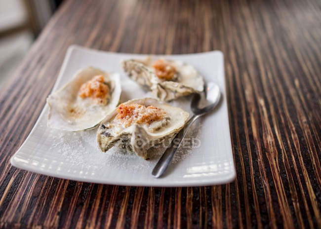 Baked oysters with spoon on white plate on table — Stock Photo