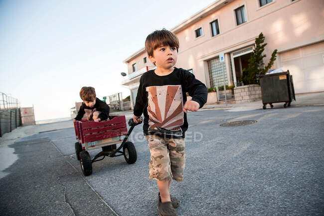 Boy pulling brother along in cart — Stock Photo