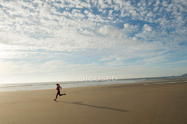 Jeune femme courant sur la plage — Photo de stock