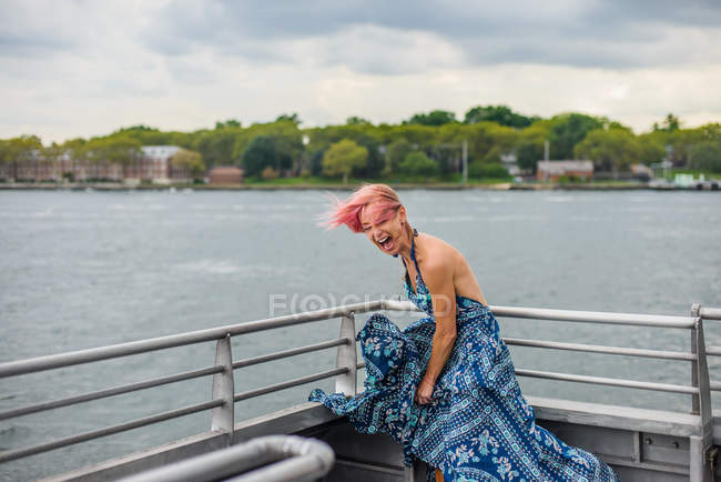Happy woman standing on boat, laughing, wind blowing dress — Stock Photo