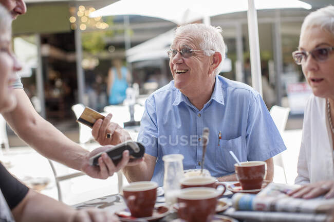 Ciudad del Cabo Sudáfrica, anciano pagando felizmente su cuenta en el restraunt con tarjeta machin - foto de stock