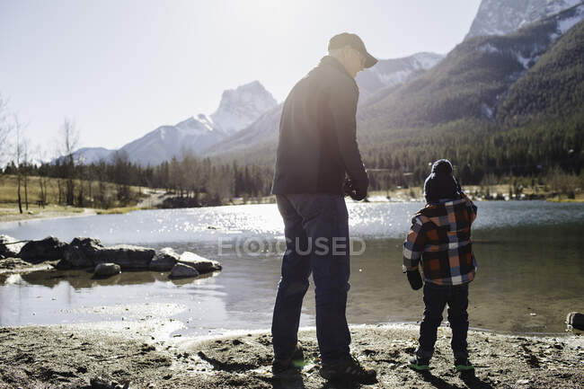 Grand-père et petit-fils au bord de la rivière, vue arrière, Montagnes Rocheuses, Canmore, Alberta, Canada — Photo de stock