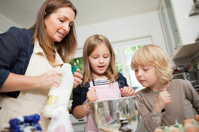 Середня доросла жінка випікає з сином і дочкою на кухні — стокове фото