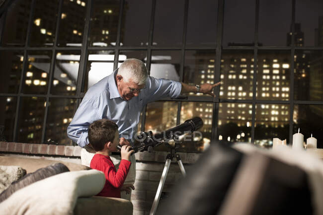 Abuelo enseñando a su nieto a usar el telescopio en casa - foto de stock