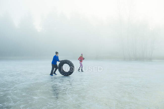 Человек катит шины по замерзшему озеру — стоковое фото