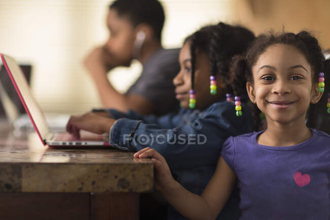 Junge und Mädchen zu Hause arbeiten mit Laptop bei den Hausaufgaben, wobei ein kleines Mädchen in die Kamera schaut — Stockfoto