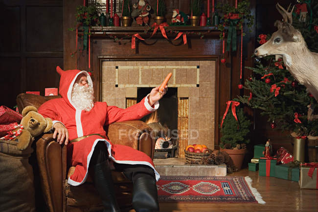 Weihnachtsmann bietet einem Hirsch eine Karotte an — Stockfoto