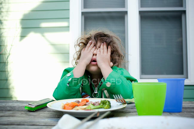 Chica joven cubriendo la cara con las manos en la mesa de picnic - foto de stock