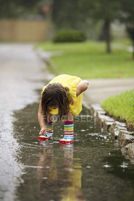 Mädchen in Gummistiefeln pflückt Blätter aus Regenpfütze — Stockfoto