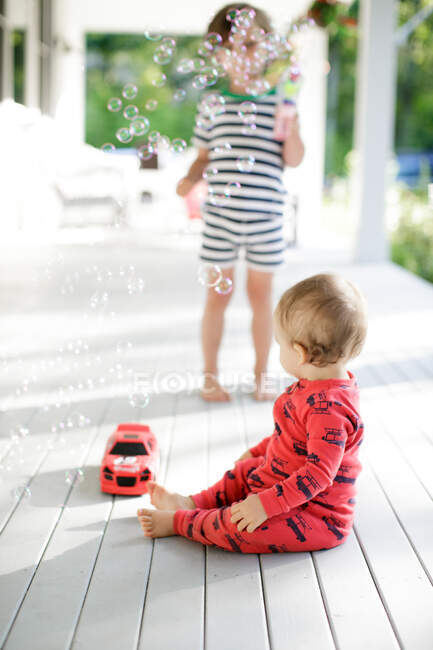 Male toddler sitting on porch watching boy blowing bubbles — Stock Photo