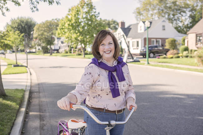 Portrait of youthful senior woman with bicycle on suburban road — Stock Photo