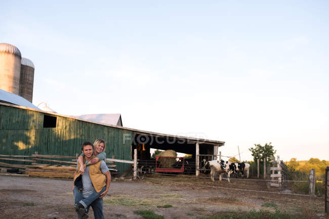 Couple on farm, man carrying woman on back — Stock Photo