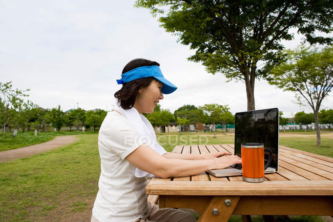 Жінка використовує ноутбук на лавці для пікніка в парку — стокове фото