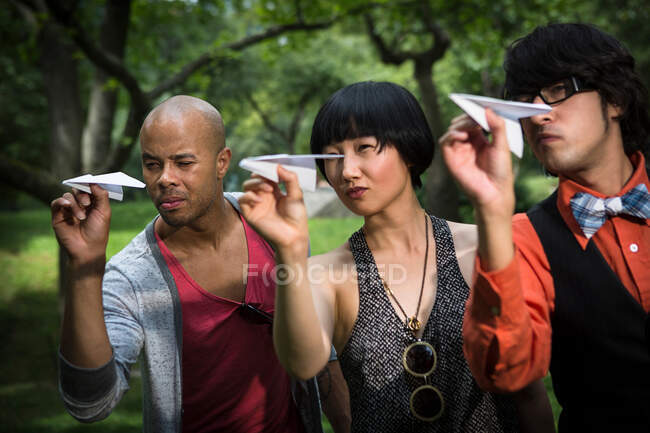 Tres amigos lanzando aviones de papel en el parque - foto de stock
