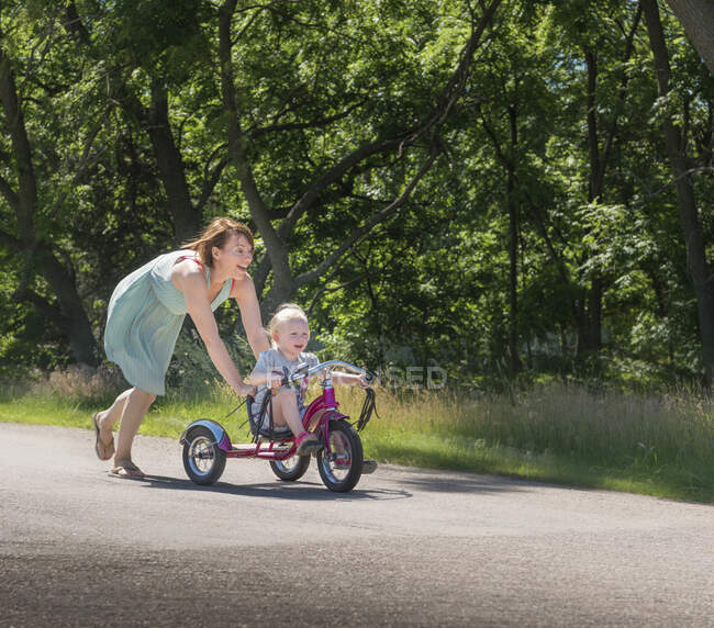 Madre empujando hija montar triciclo - foto de stock