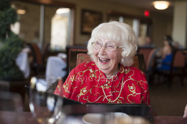 Пожилая женщина, сидящая за столом в ресторане, смеется — стоковое фото