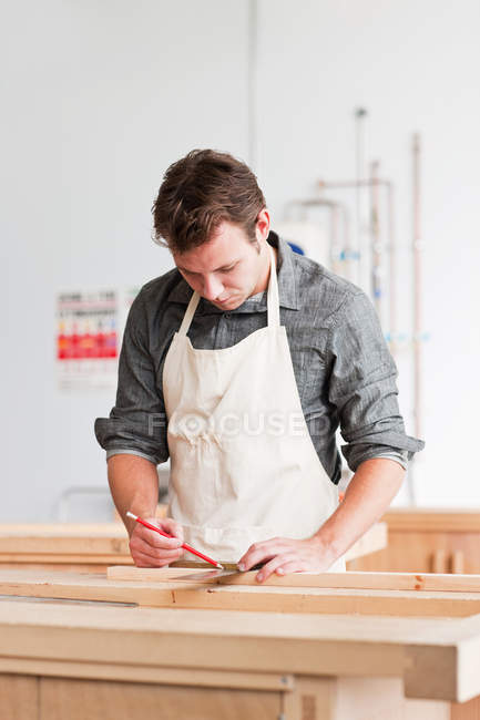 Carpinteiro medindo prancha de madeira na oficina — Fotografia de Stock