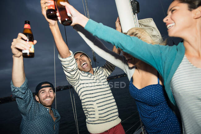 Друзі тости з пляшками пива на вітрильному човні — стокове фото