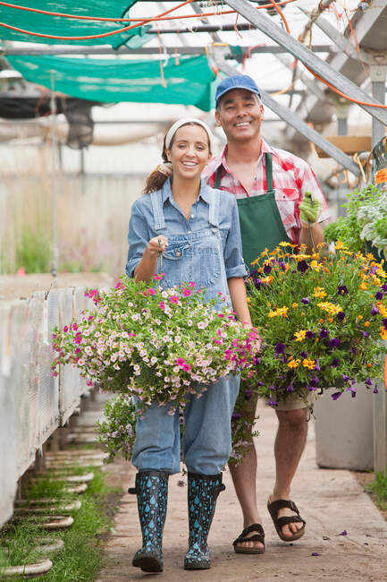 Young woman and mature man walking with hanging baskets in garden centre — Stock Photo