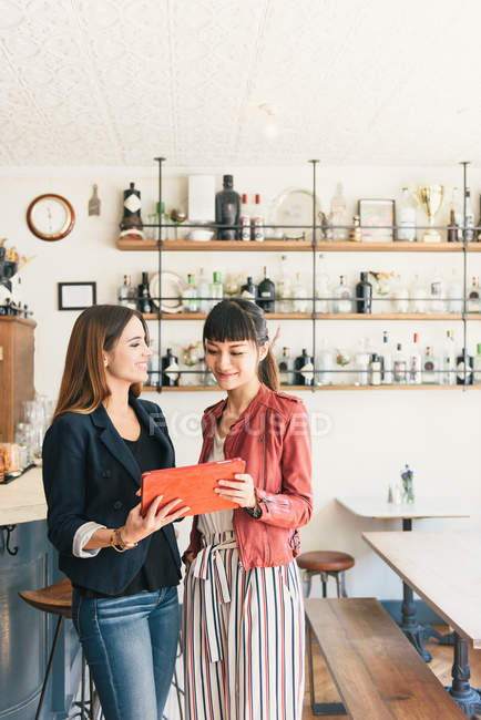 Two young women looking at digital tablet in cocktail bar — Stock Photo