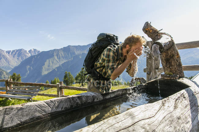 Joven caminante lavando la cara en canal rústico, Karthaus, Val Senales, Tirol del Sur, Italia - foto de stock