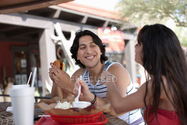 Young couple eating in outdoor cafe, smiling — Stock Photo
