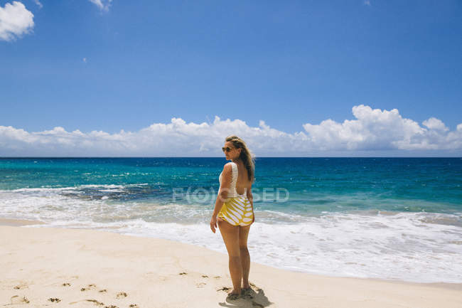 Mujer con traje de baño y mirando hacia atrás desde la playa de Makua, Hawaii, EE.UU. - foto de stock