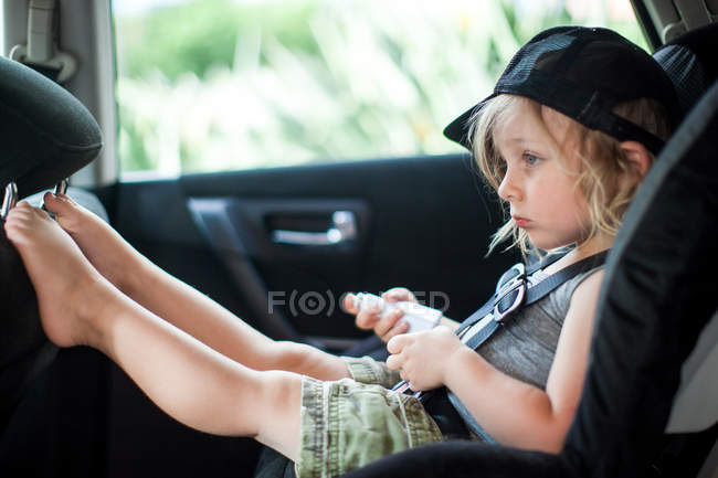 Молодий хлопець сидить на дитячому сидінні на задньому сидінні автомобіля, нудний вираз — стокове фото