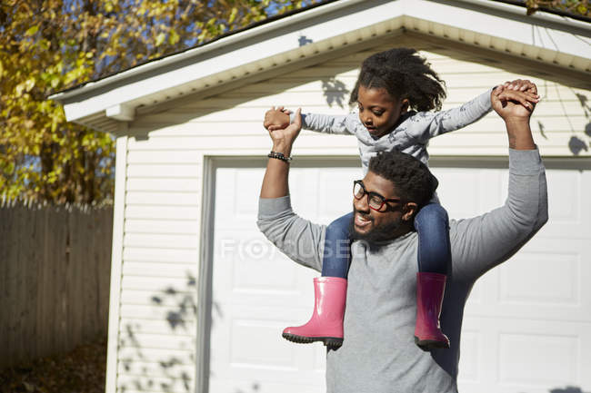 Mature man carrying daughter on shoulders by residential garage — Stock Photo