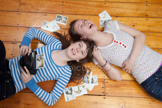 Girls lying on floor with camera, surrounded by photographs — Stock Photo