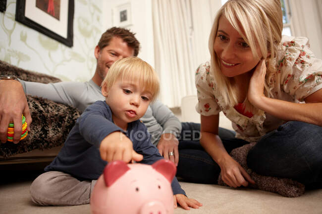 Vater, Mutter und Sohn legen Münzen in Sparschwein — Stockfoto