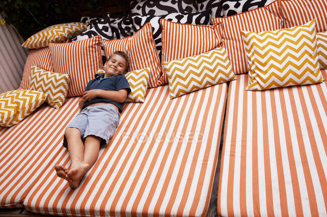 Boy relaxing on striped outdoor  furniture with cushions — Stock Photo