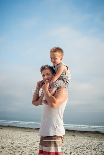 Young man carrying son on shoulders on beach — Stock Photo