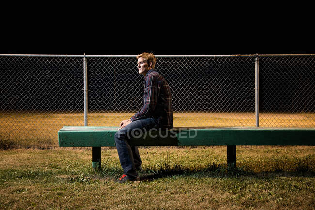 Pensive young man sitting on bleachers at night — Stock Photo