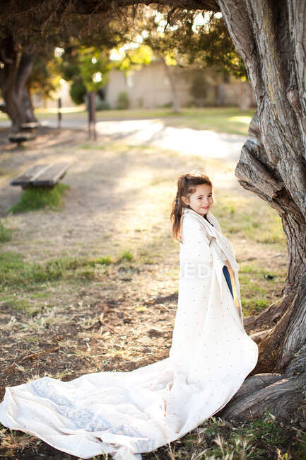 Portrait of girl wrapped in sheet under tree — Stock Photo