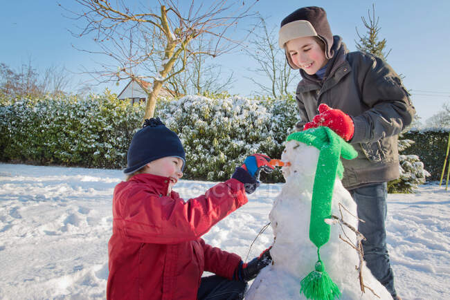 Chicos haciendo muñeco de nieve en el jardín - foto de stock