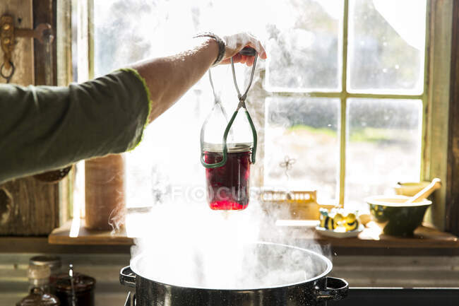 Frauenhände entfernen Rote-Bete-Marmeladenglas aus dampfendem Topf — Stockfoto