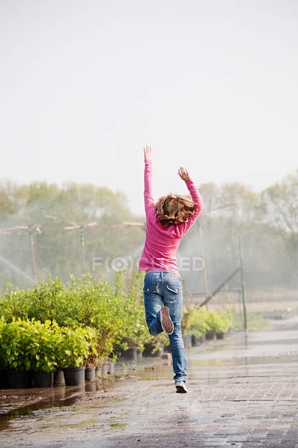 Vista trasera de la niña saltando a lo largo del camino en el vivero de plantas - foto de stock