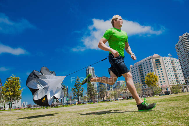 Молодий чоловік біжить в міському парку з парашутом — стокове фото