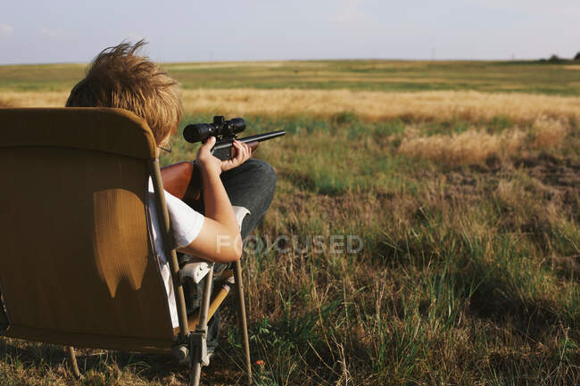 Boy on rural landscape pointing shotgun into distance — Stock Photo