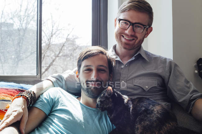 Мужская пара отдыхает на диване вместе с кошкой — стоковое фото