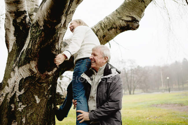 Hombre mayor ayudando a la mujer a trepar árbol en el parque - foto de stock